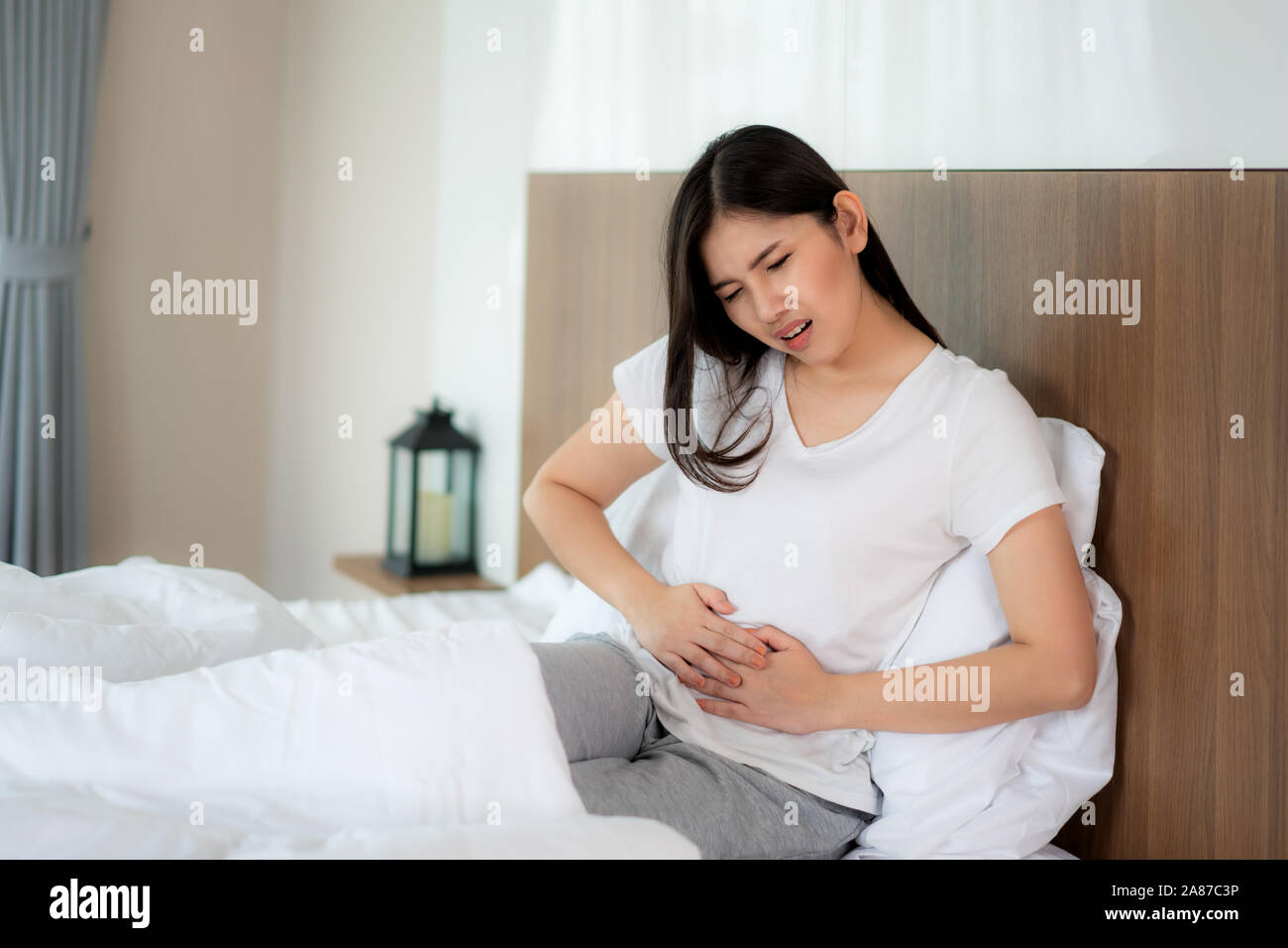 Donna asiatica infelice giacente sul letto cercando di malessere, soffre di mal di stomaco in camera da letto, stomachache a causa delle mestruazioni e mangiare rovinato fo Foto Stock