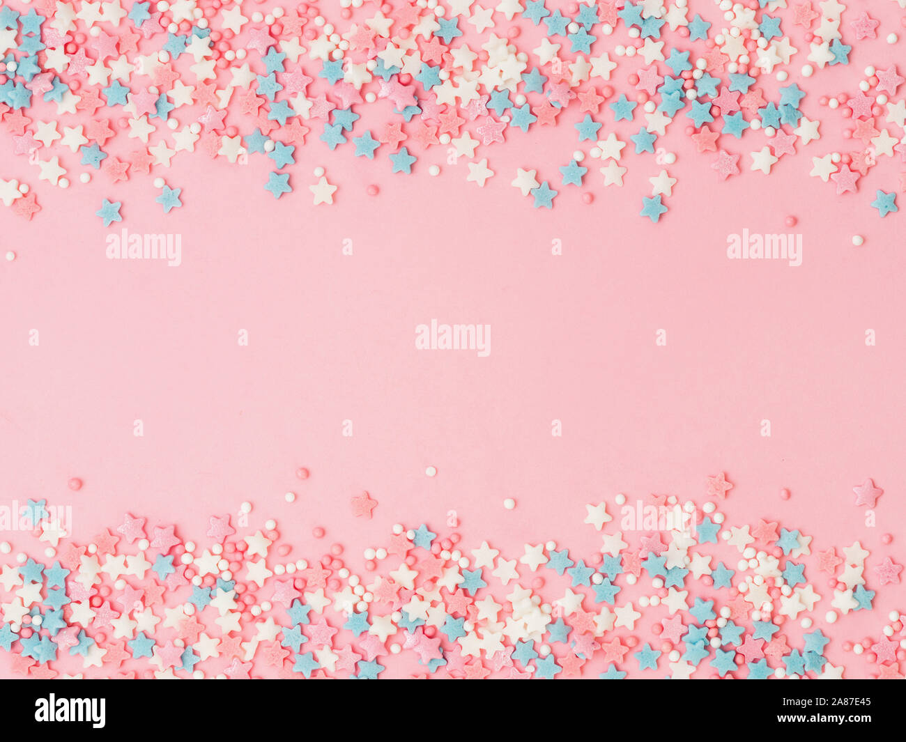 Festosa cornice di confine del pastello colorato spruzza su sfondo rosa con copia spazio nel centro. Cospargere di zucchero Punti e stelle, decorazione per torte e pasticceria. Vista superiore o laici piatta Foto Stock