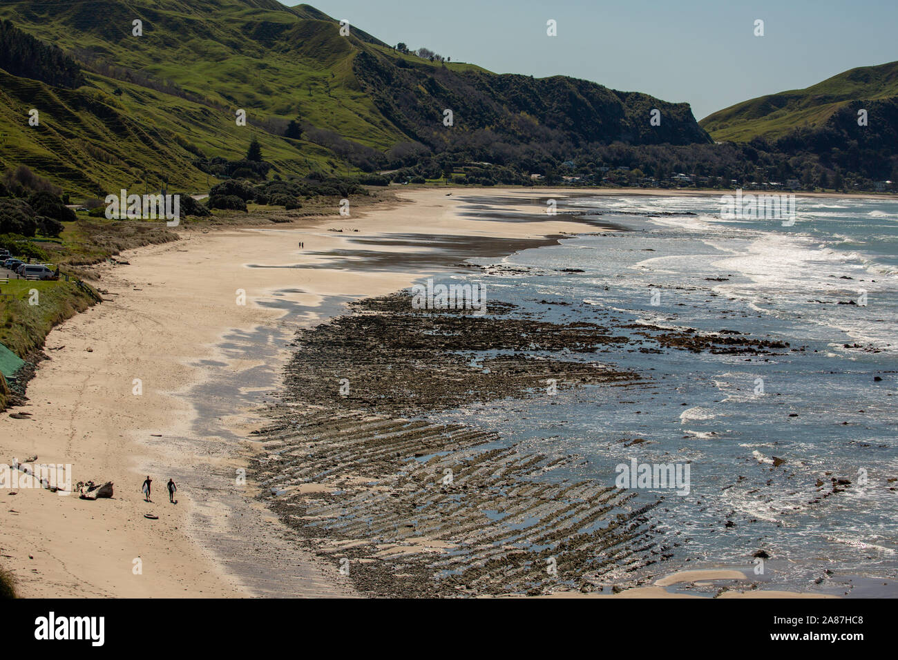Due surfisti sconosciuto a piedi lungo la spiaggia con la bassa marea con le rocce esposte Foto Stock