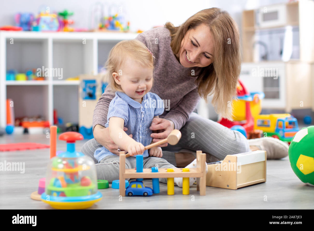 Allegro baby giocare con giocattoli con felice madre nella nursery room Foto Stock