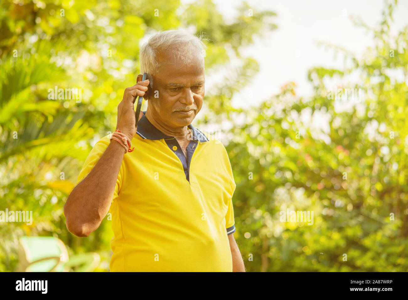 L'uomo anziano occupato in mobile - sani indiano senior sul telefono outdoor presso park, Mattina - Happy genitore maschile parlando al telefono. Foto Stock