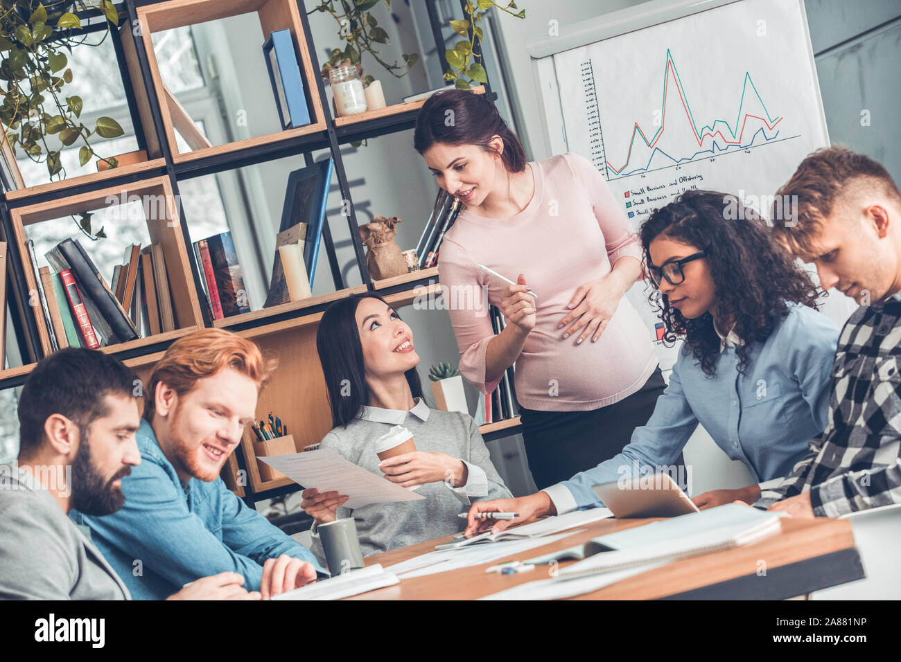 Startupers lavorando insieme a Office seduta che mostra una donna incinta collega piano di progetto allegro Foto Stock