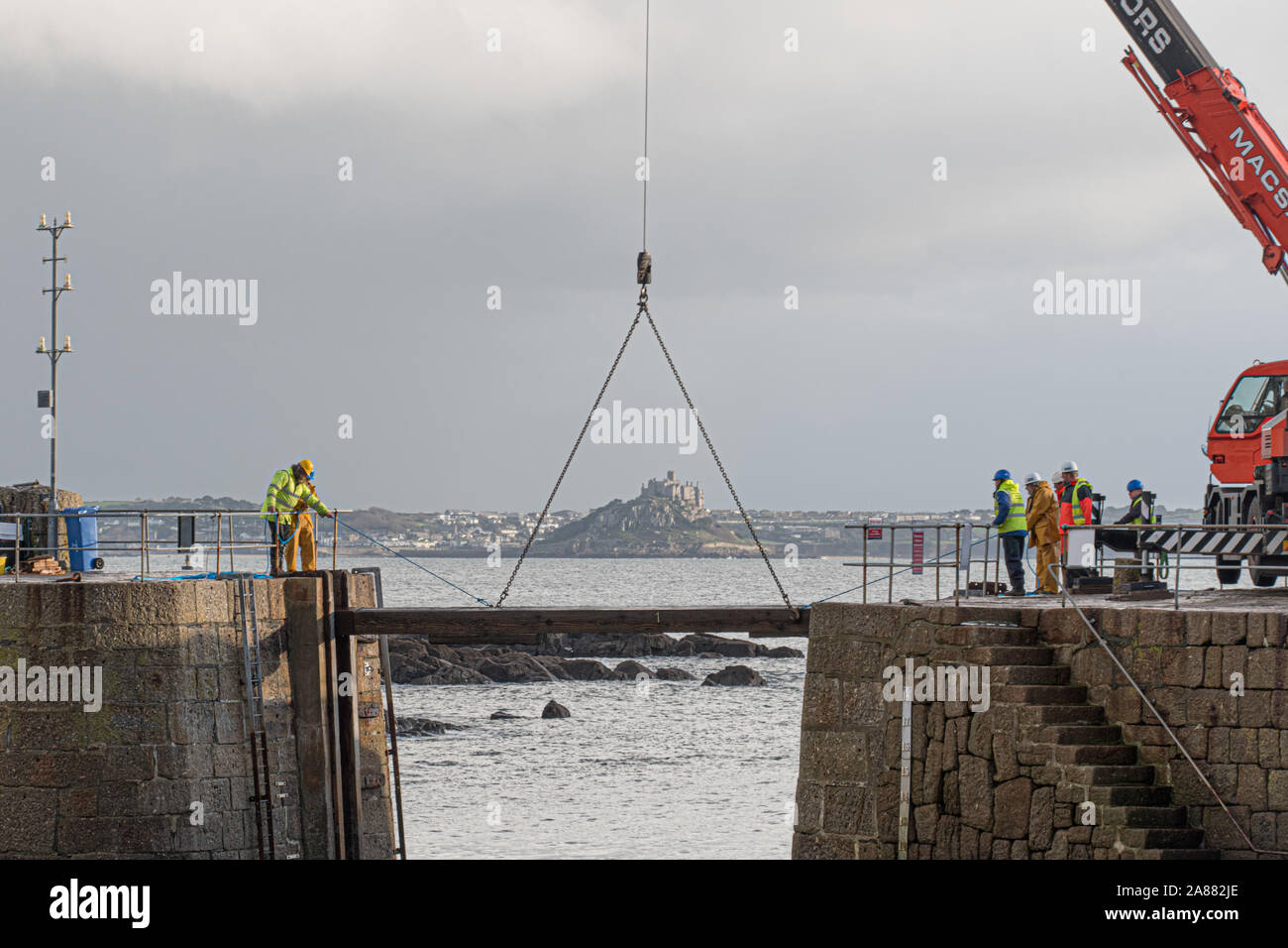 Mousehole, Cornwall, Regno Unito, 7 novembre 2019. Regno Unito Meteo. Ogni anno giant degli spessori di legno vengono abbassati delicatamente nell'apertura di Mousehole Harbour, per proteggerlo dalle tempeste invernali. Visto in background St Michaels Mount a Marazion. Simon credito Maycock / Alamy Live News. Foto Stock