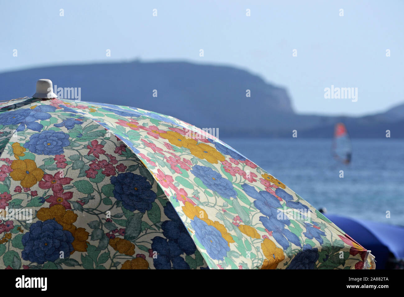Close-up di decorazioni colorate di un ombrellone. Il mare mediterraneo e un windsurf sullo sfondo Foto Stock