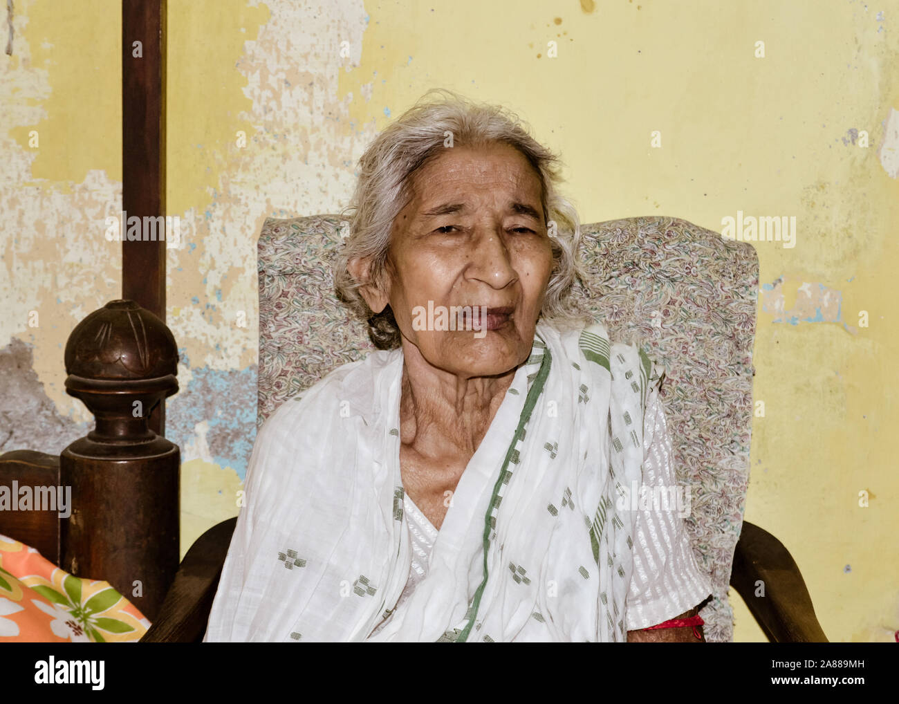 Ritratto di sorridere Active senior asiatici ed etnia indiana donna di 82 anni seduti su una sedia appoggiata a casa mentre guardando la fotocamera. Foto Stock
