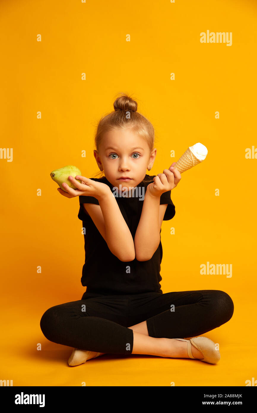 Perplesso little ballerina scegliendo tra pera e gelato Foto Stock