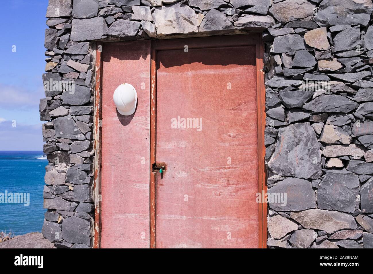 Lavoratore bianco casco appeso su una vecchia porta di legno di una casa in pietra (Achadas Da Cruz, Madeira, Portogallo, Europa) Foto Stock