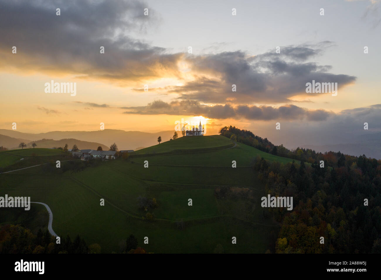 Vista aerea delle colline, colorato e la foresta Sv Sobota chiesa. Slovenia il tramonto in autunno Foto Stock