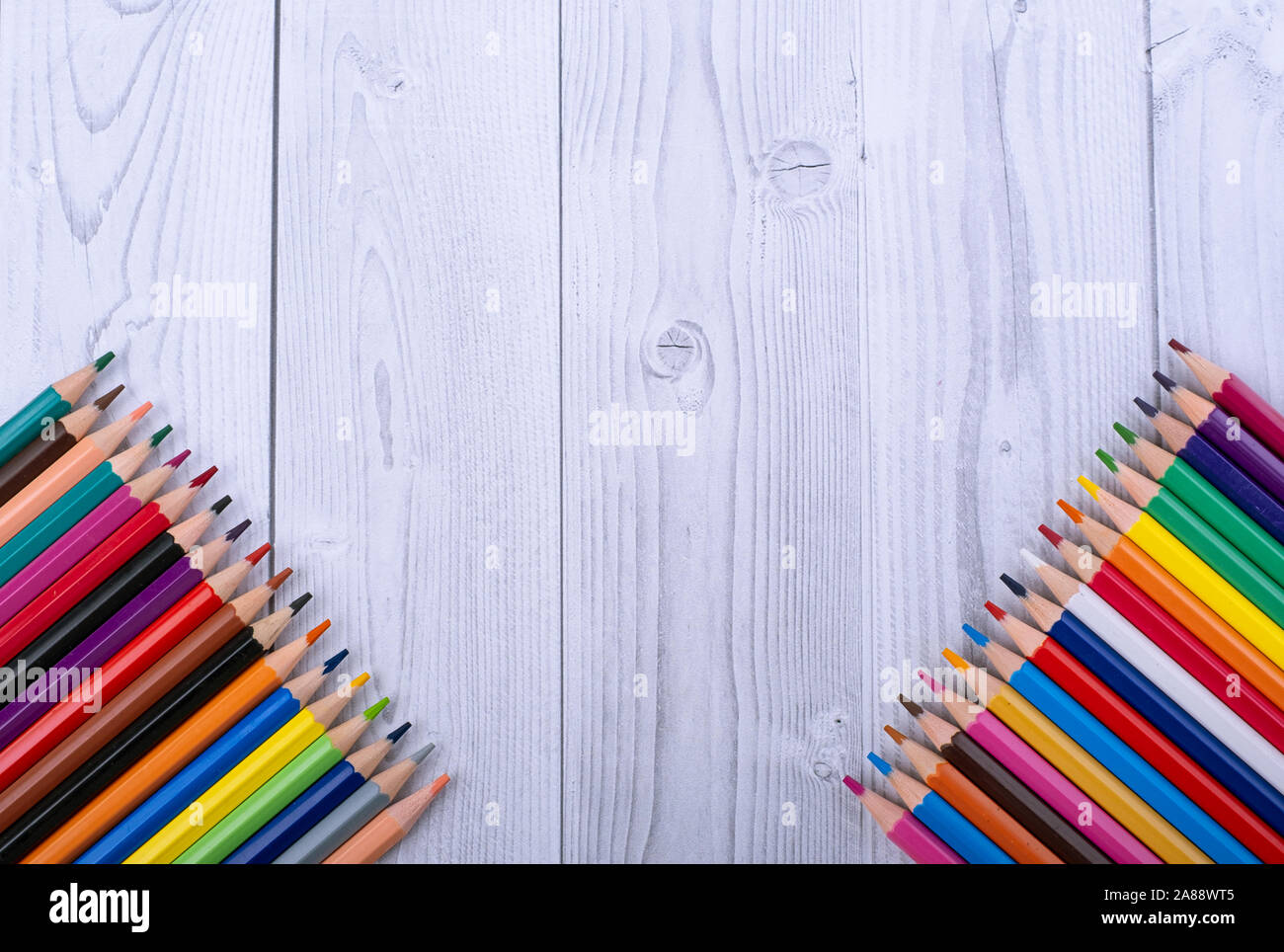 In legno colorato matite, negli angoli inferiori del bianco e del grigio Sfondo di legno Foto Stock