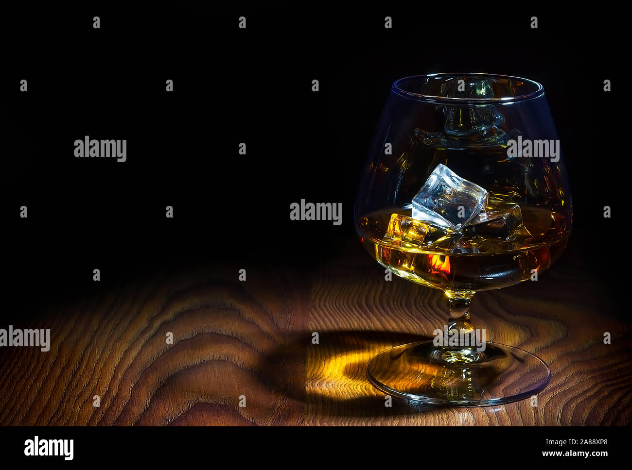 Un bicchiere di cognac con cubetti di ghiaccio in un incantevole forma attraente, in piedi su una superba bellezza superficie Foto Stock