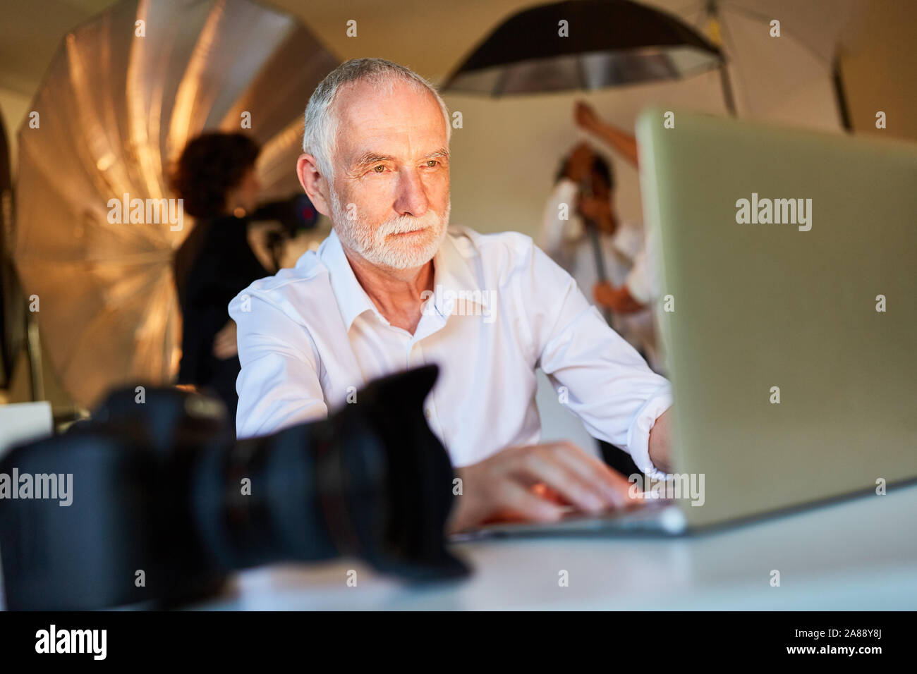 Fotografo senior presso il computer portatile in photo studio durante l'editing di immagini Foto Stock