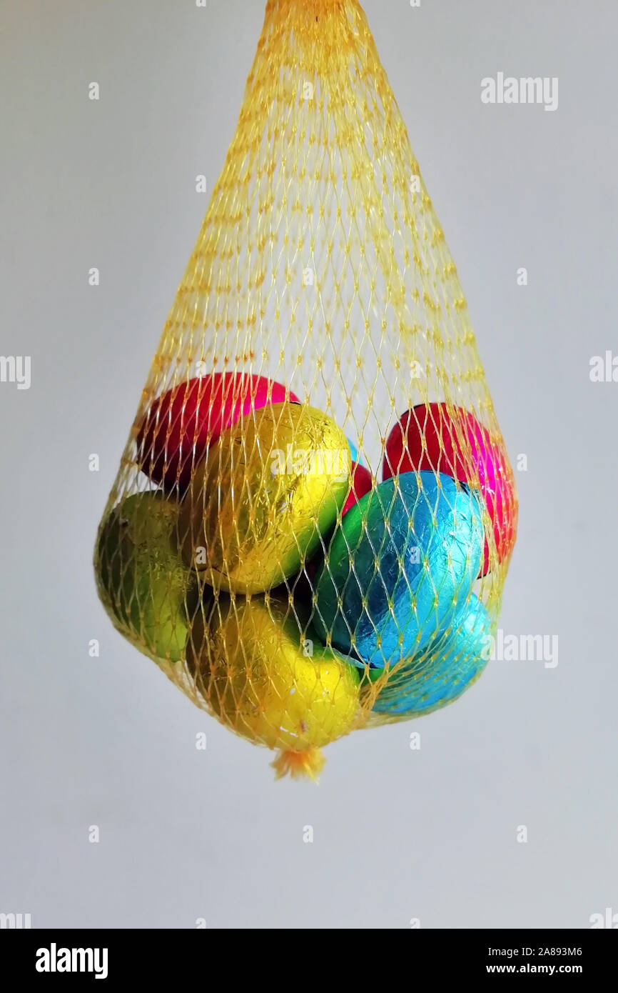 Multi uova colorate avvolto nel foglio piegato in modo da formare una maglia gialla. Uova di cioccolato in un sacchetto per i bambini. Foto Stock