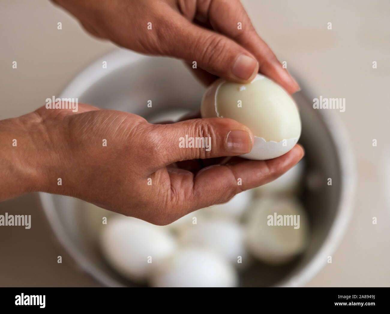 Primo piano della mano di donna indiana peeling un uovo sodo in cucina. Ricetta uovo processo di preparazione per il concetto di sfondo. Foto Stock