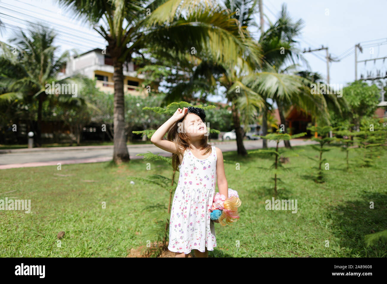 Giovani caucasici bambina in piedi con la bambola vicino a palmi in background. Foto Stock