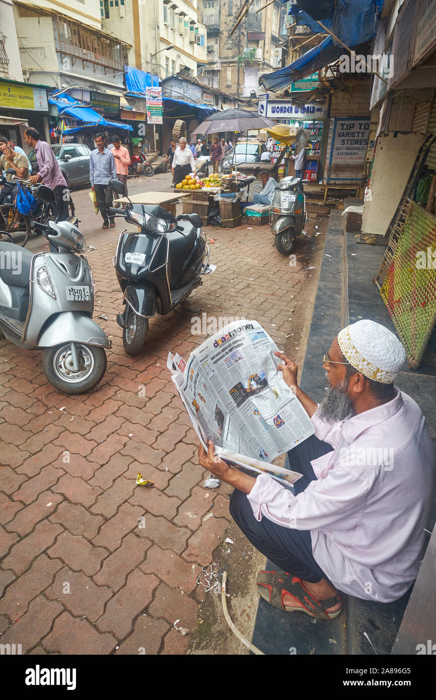 Un Bohra musulmano in una corsia in il musulmano dominato Bhendi Bazar area di Mumbai, India, la lettura di notizie finanziarie nel giornale locale del DNA. Foto Stock