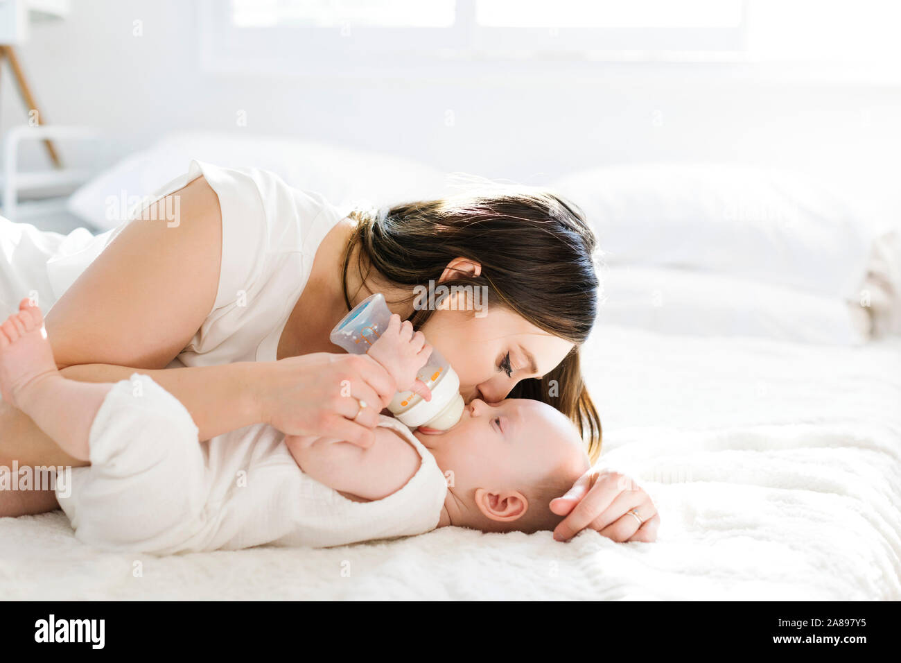 Madre baciando la guancia di suo figlio mentre beve una bottiglia di latte Foto Stock
