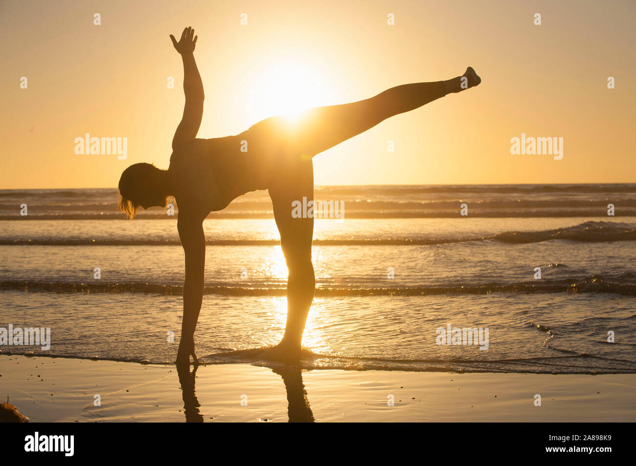 Silhouette di donna che fa yoga sulla spiaggia al tramonto Foto Stock