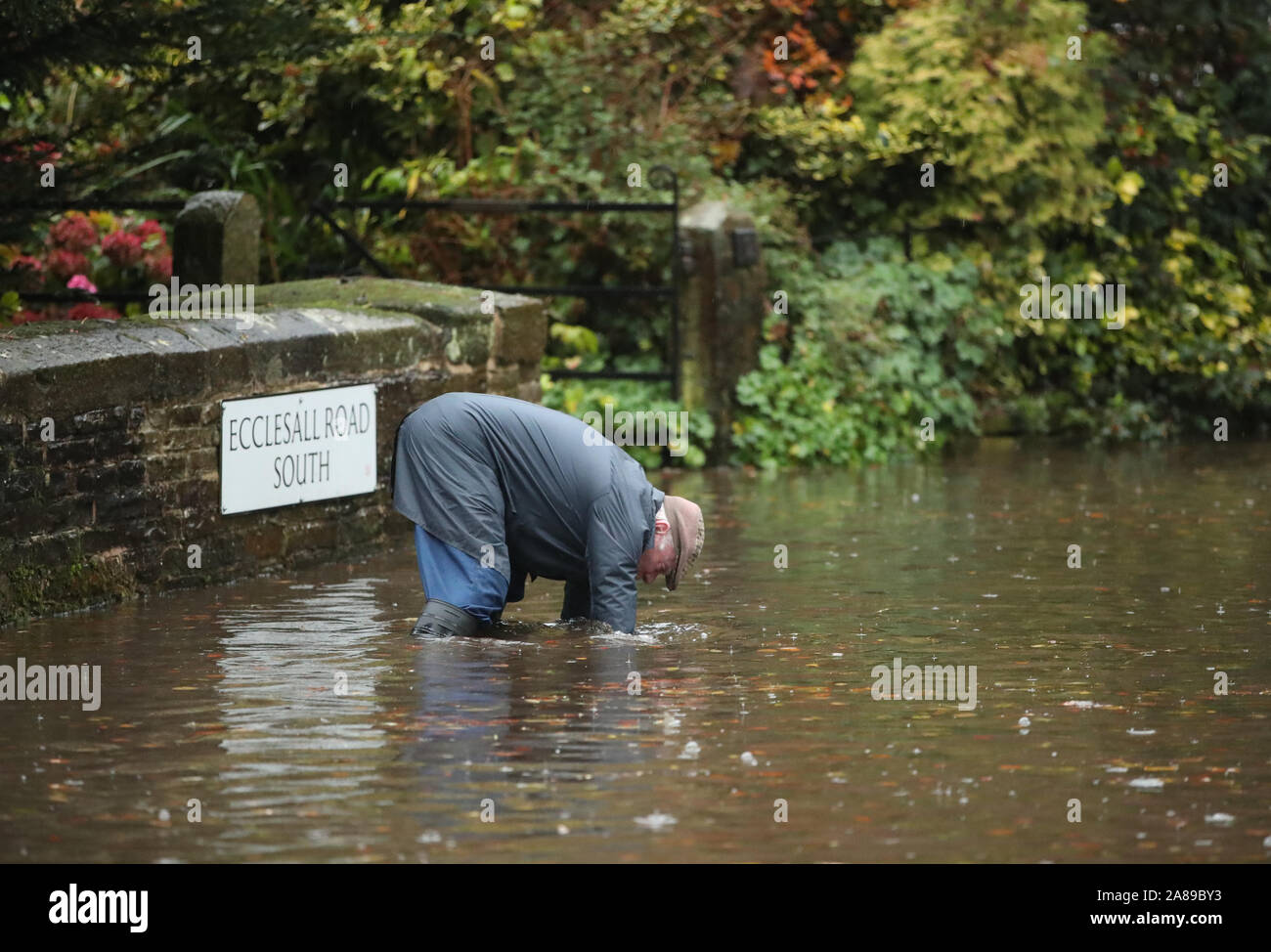 Un uomo tenta di sbloccare un drenaggio su una strada allagata in Whirlow, Sheffield, dopo piogge torrenziali nella zona. Foto Stock