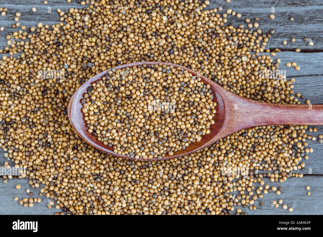 Semi di senape nel piatto di legno con il cucchiaio sul tavolo. La cottura di porridge, cibo sano Foto Stock