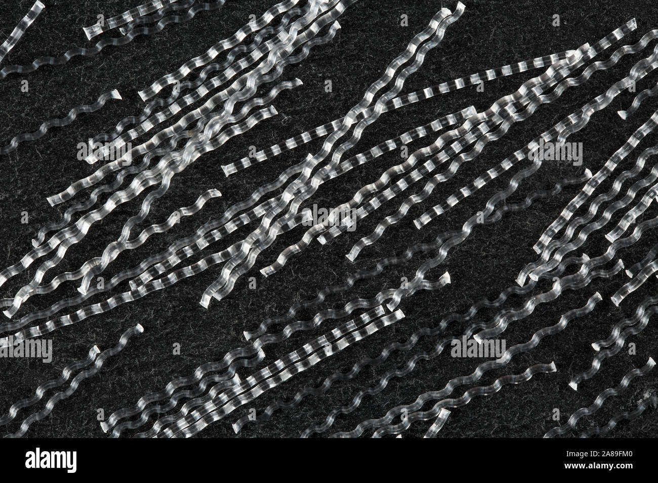 Extreme close up, vista dall'alto in basso di macro sinusoidale in polipropilene fibre per rinforzo del calcestruzzo su pietra nera dello sfondo. Industria di costruzione Foto Stock