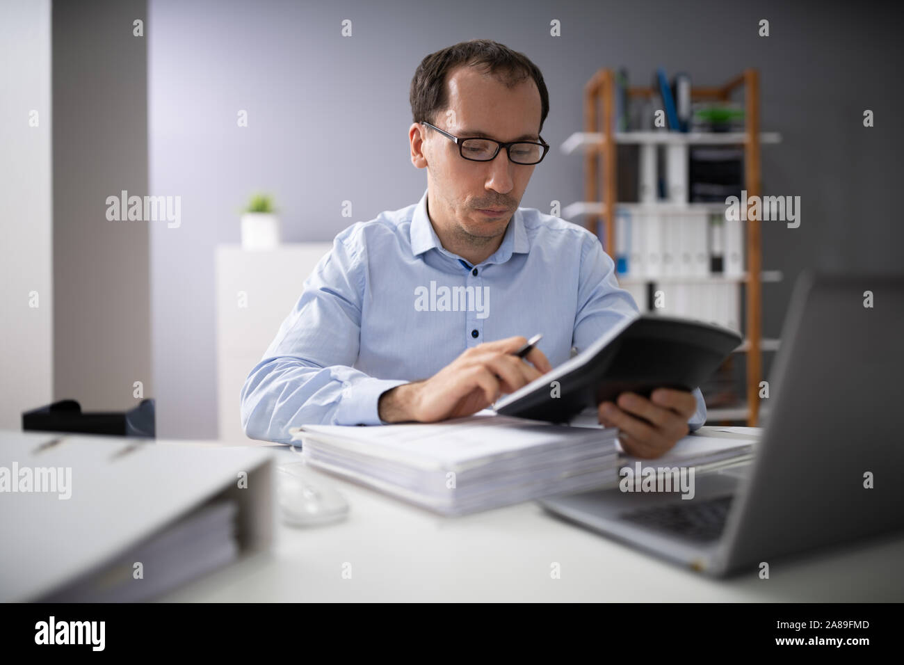Oltre la spalla di imprenditore il calcolo di fatture utilizzando la calcolatrice Foto Stock