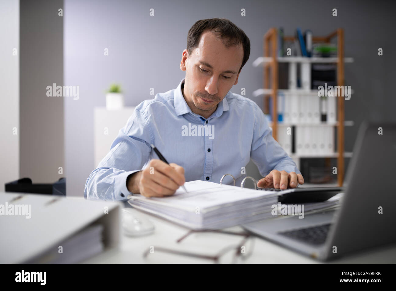 Oltre la spalla di imprenditore il calcolo di fatture utilizzando la calcolatrice Foto Stock