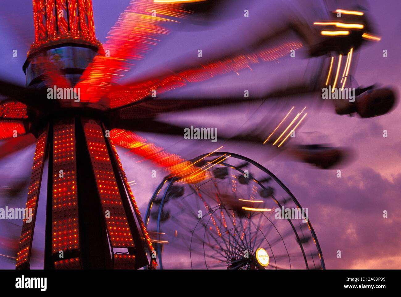 Whirling, illuminati al neon ride di carnevale al crepuscolo Foto Stock