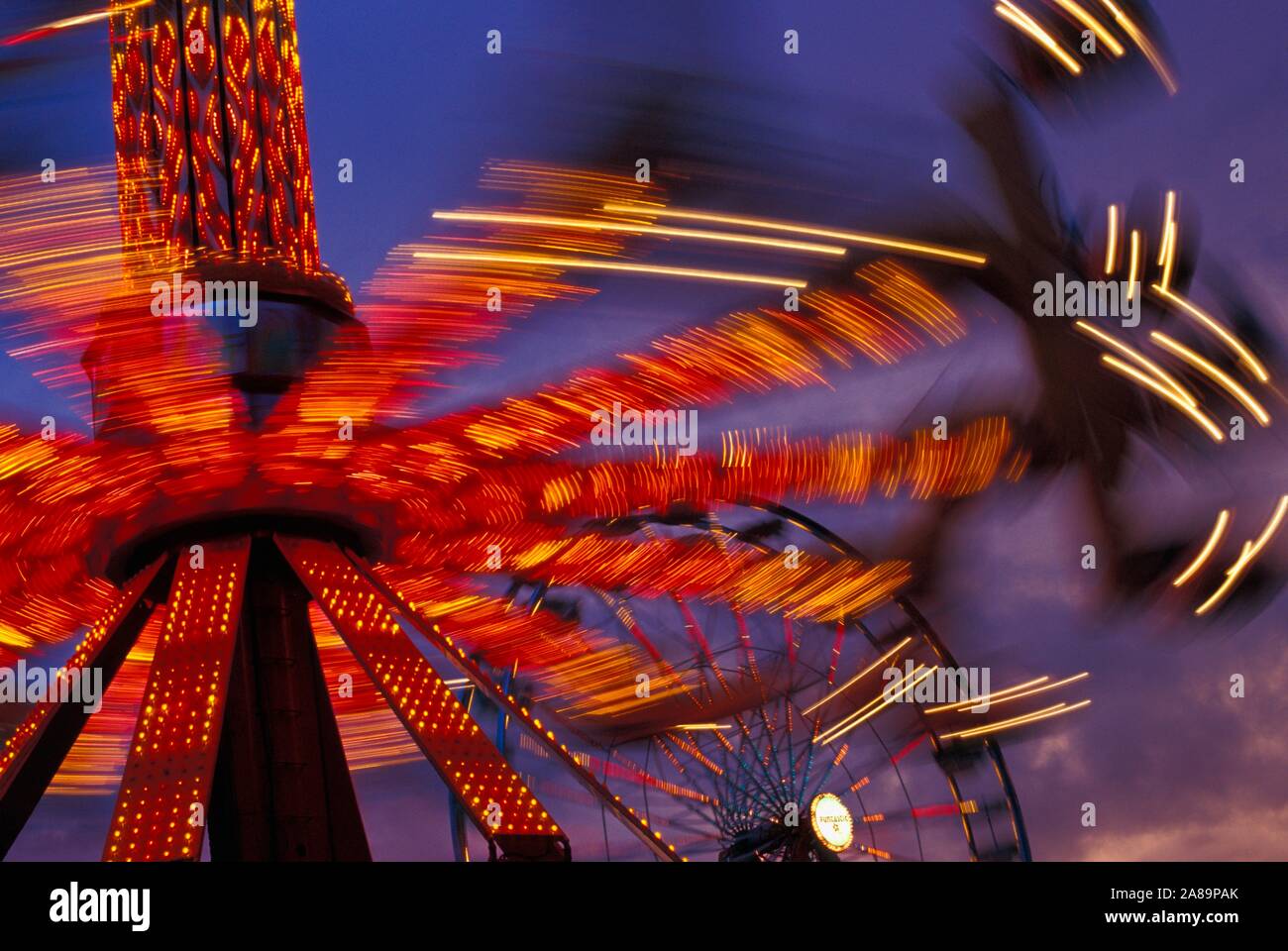Whirling, illuminati al neon ride di carnevale al crepuscolo Foto Stock