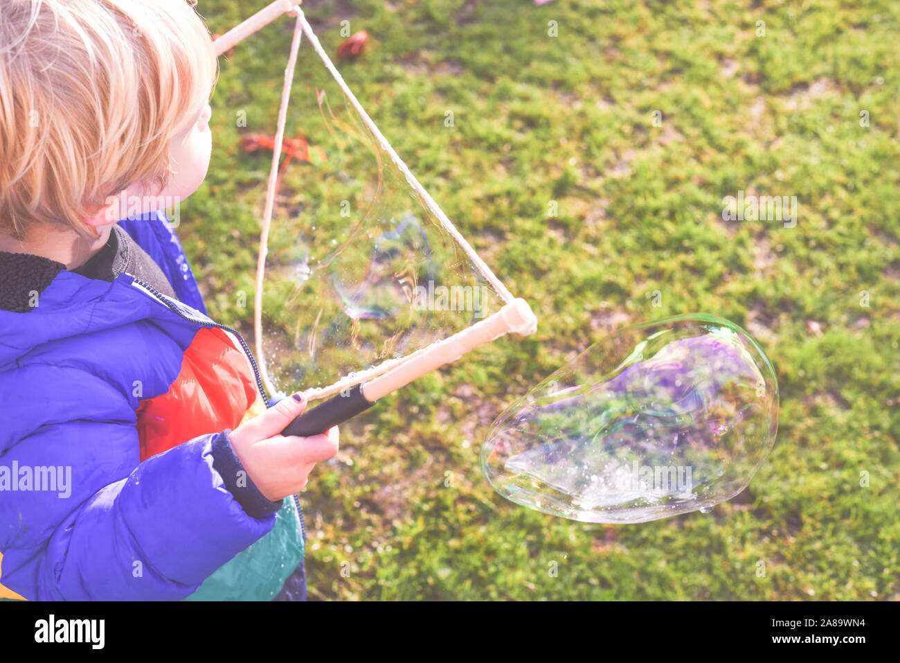 Bambini che giocano al di fuori in un giardino durante il giorno con bolle è felice e in esecuzione Foto Stock