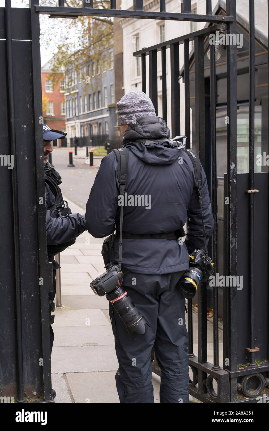 Vista posteriore dei maschi di premere fotografo essendo controllati presso la polizia cancello di sicurezza prima di entrare a Downing Street a Londra durante la campagna elettorale del 2019. Foto Stock