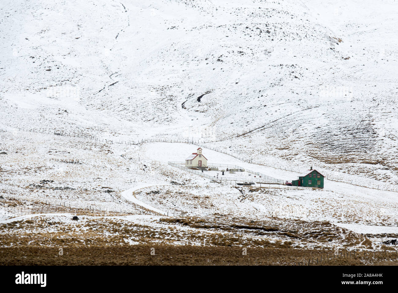 Un bianco chiesa di legno e un blu agriturismo sedersi da solo su una collina innevate in Islanda Foto Stock
