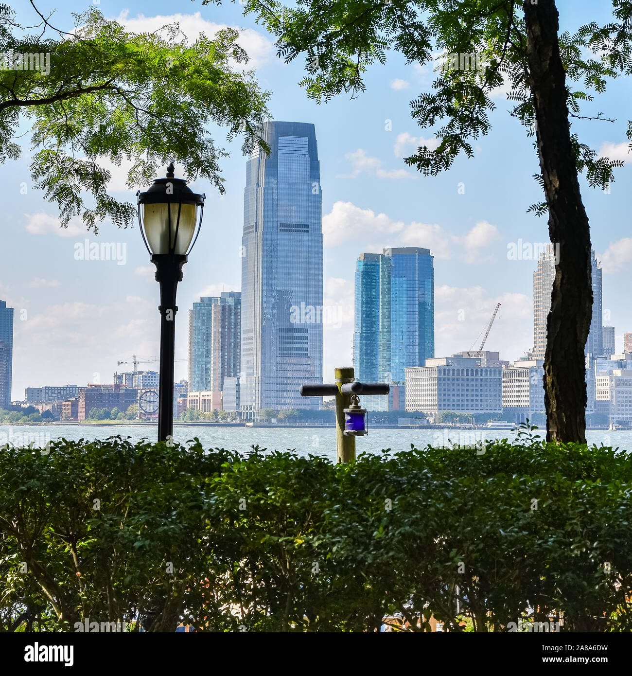 New Jersey skyline da Battery Park in una giornata di sole. Paesaggio urbano vista attraverso gli alberi e lampione. Città e il concetto di viaggio. Manhattan, New York City, U Foto Stock