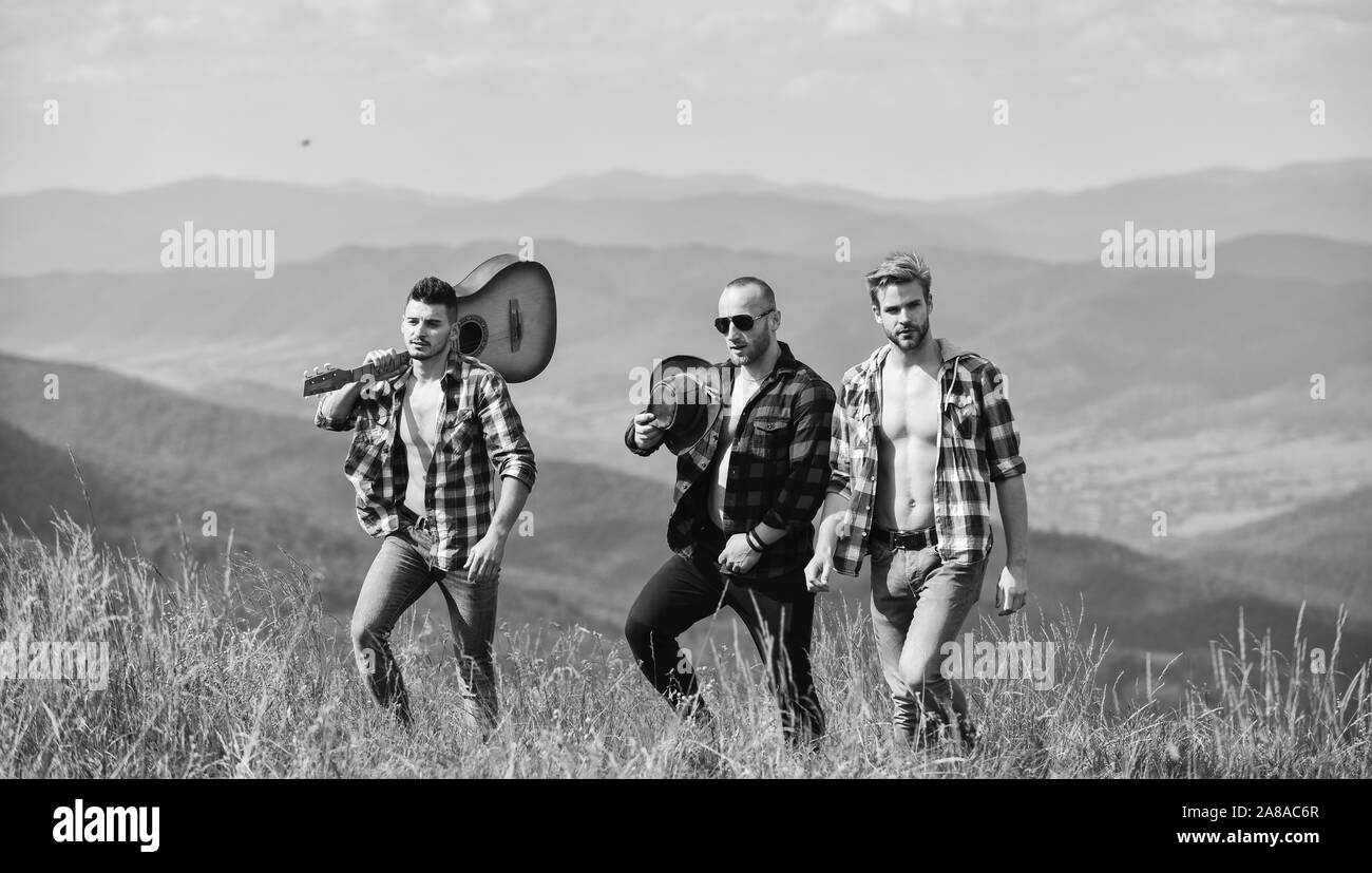 Un gruppo di giovani in camicie a scacchi camminare insieme sulla cima della montagna. I turisti escursionismo concetto. Escursioni con gli amici. Gentile ragazzi con la chitarra escursionismo sulla giornata di sole. Godendo la libertà insieme. Foto Stock