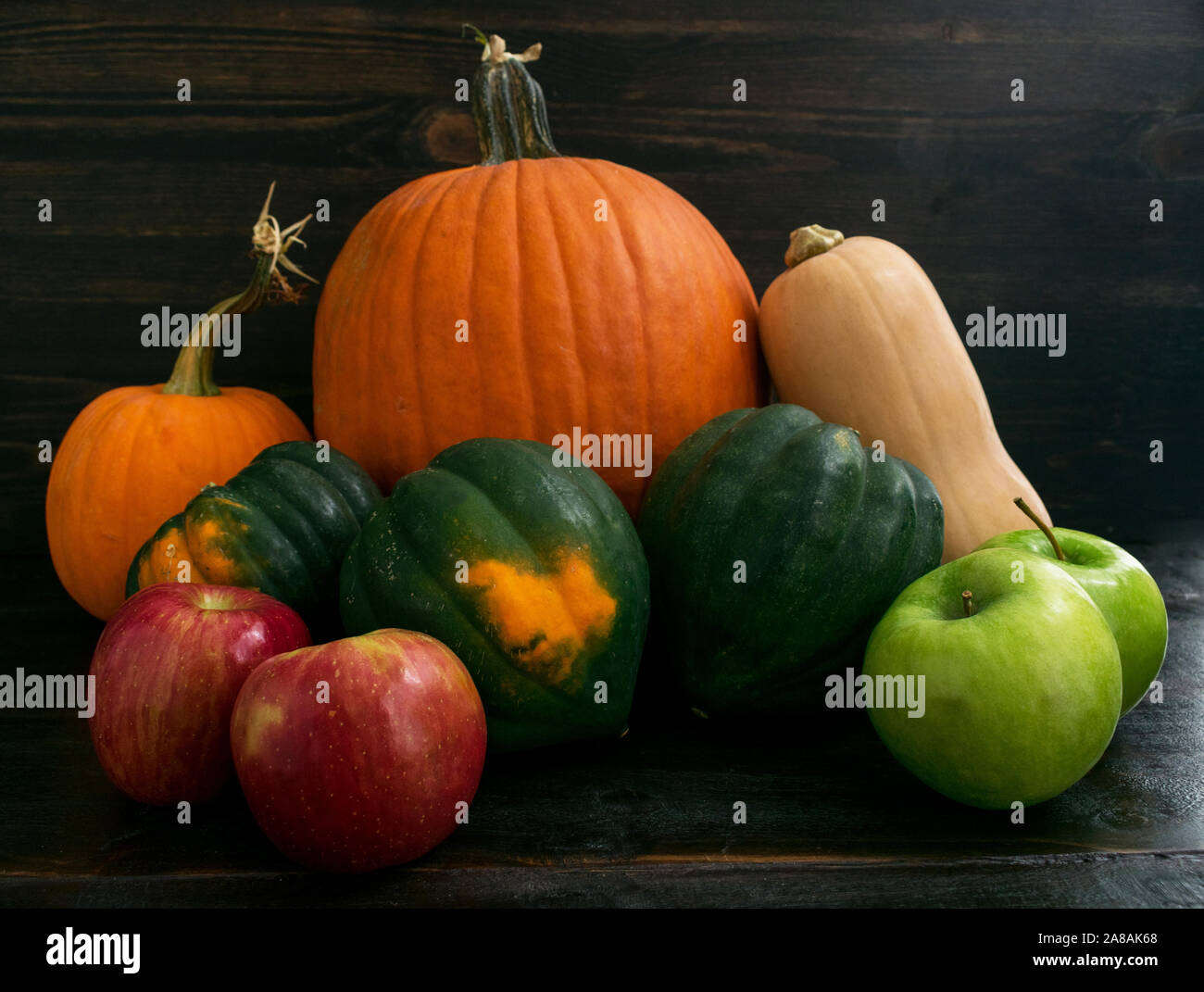 Raggruppamento di rustico di mele, acorn squash, zucca, e zucche al buio su un sfondo di legno Foto Stock