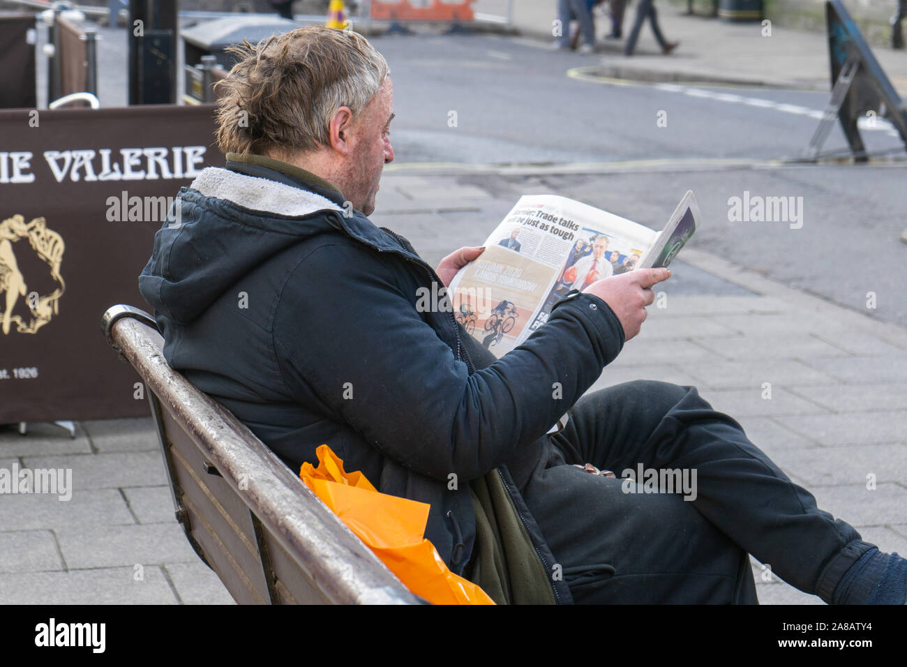 Un uomo seduto su una panchina leggendo un giornale Foto Stock