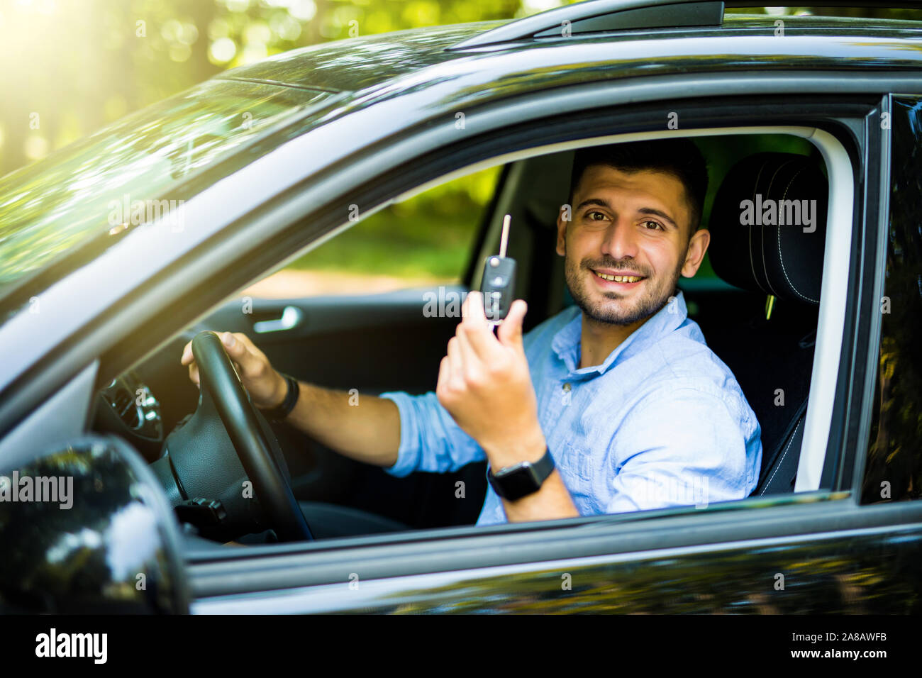 Giovane uomo seduto all'interno di nuove auto con chiavi. Sorridente Foto Stock