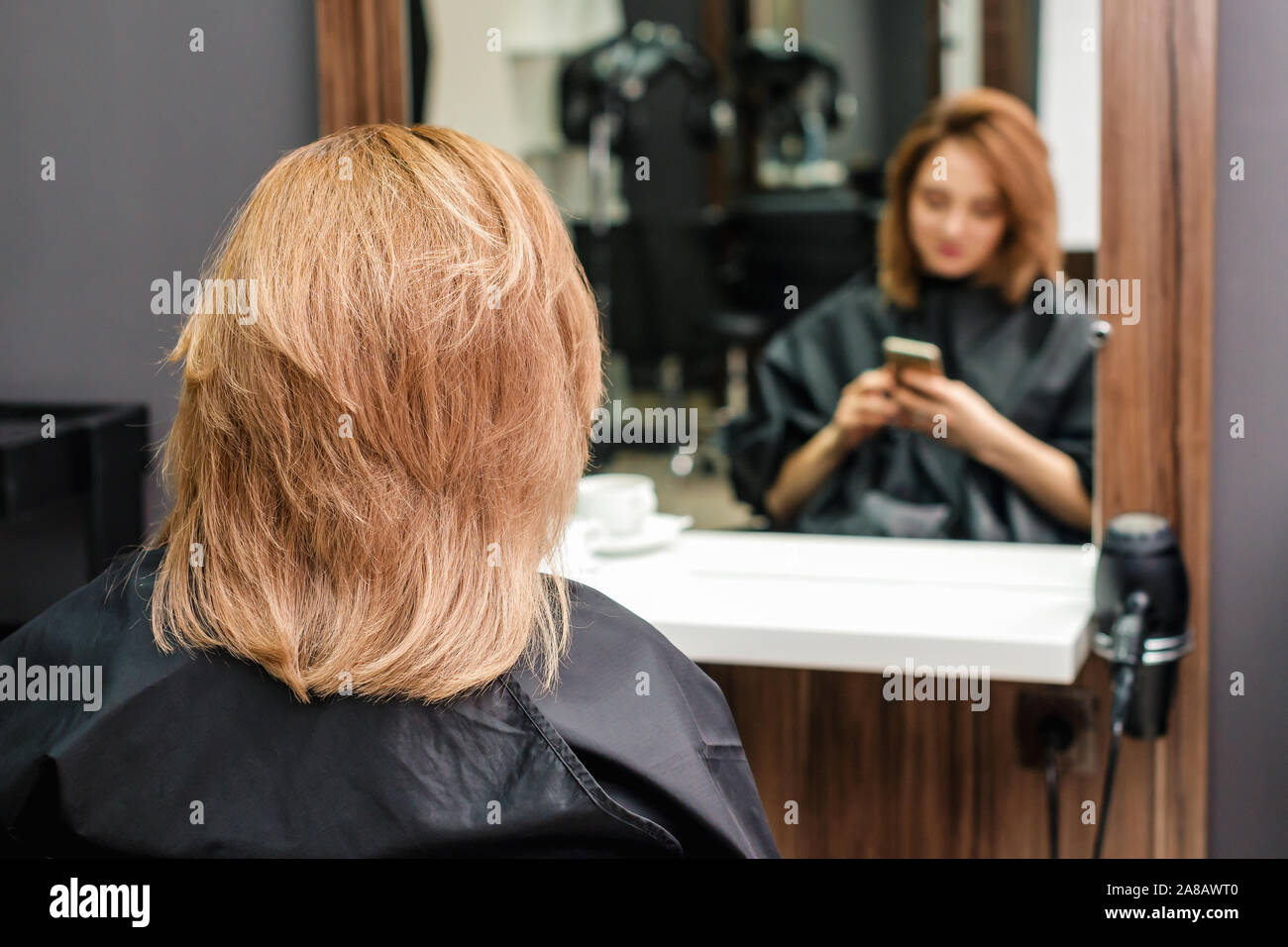 Giovane donna con nuova acconciatura è seduta davanti allo specchio nel  salone di parrucchiere vista posteriore Foto stock - Alamy