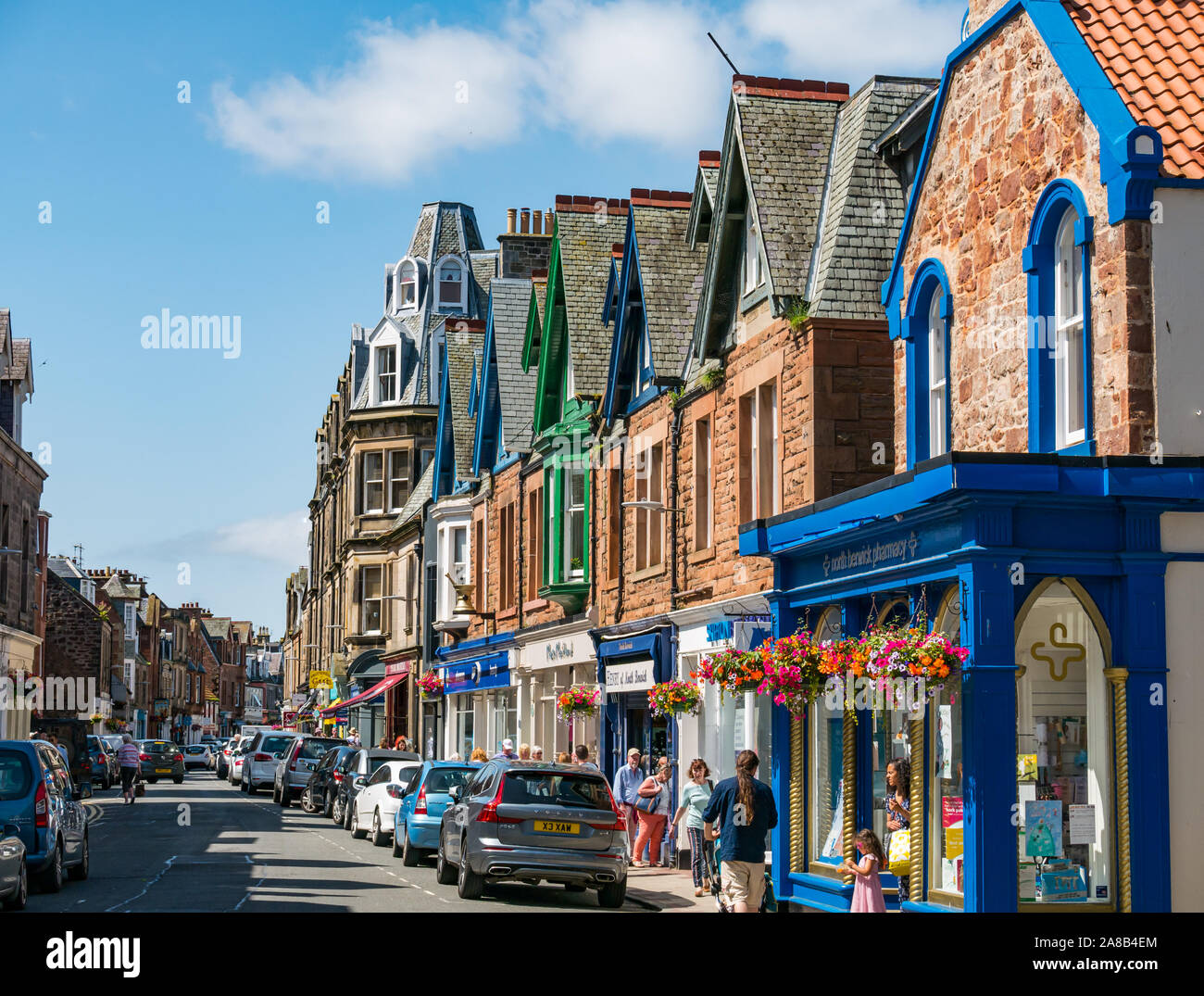 Trafficata stradina con macchine parcheggiate e la gente lo shopping, High Street, North Berwick, East Lothian, Scozia, Regno Unito Foto Stock
