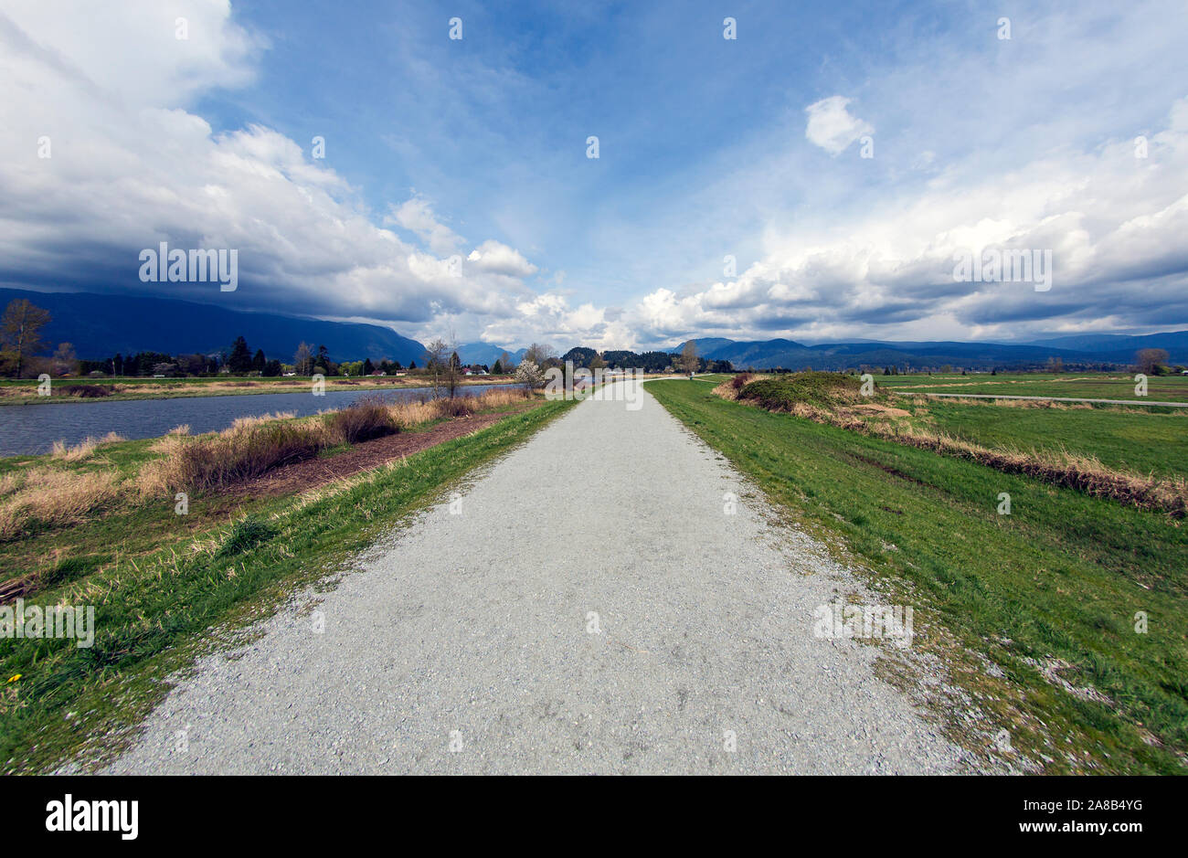 Incredibile angolo ampio paesaggio con dyke e nuvole come linee principali, concetto di lunga strada da percorrere. Golden Ears montagna, Pitt River, Pitt Meadows, Canada Foto Stock