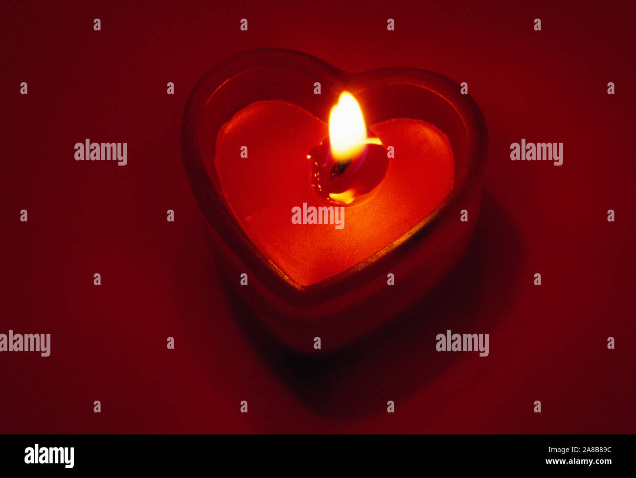 Fiamma ardente nel cuore di candela sagomata contro lo sfondo rosso Foto Stock