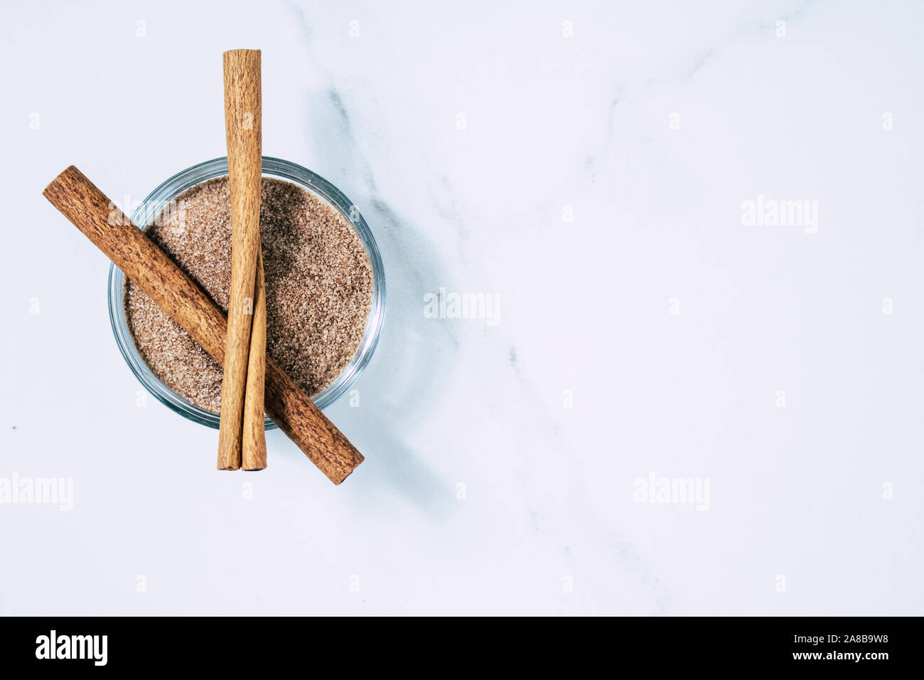 Bastoncini di cannella e una piccola ciotola di zucchero alla cannella su marmo Bianco Counter Foto Stock