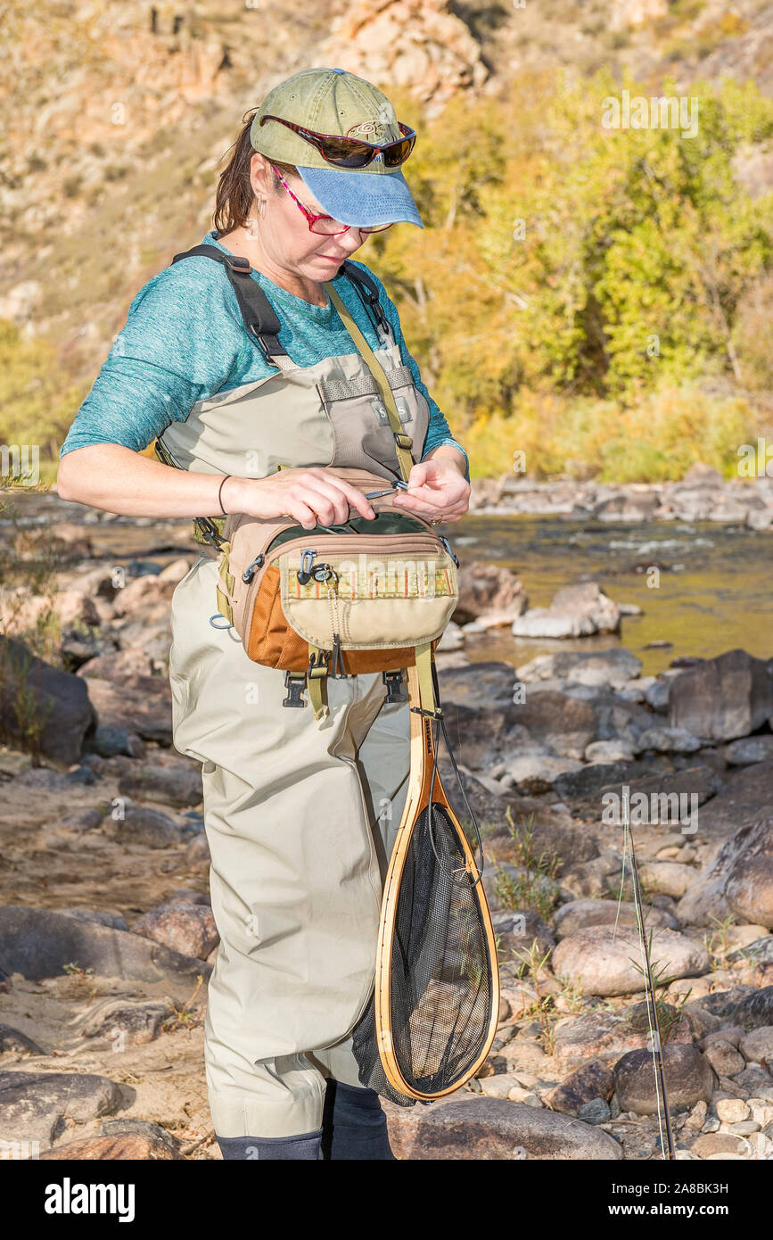 Una donna che prepara la sua canna da pesca con la linea e un gancio come ella capi sulla Poudre fiume per un pomeriggio di pesca. Foto Stock