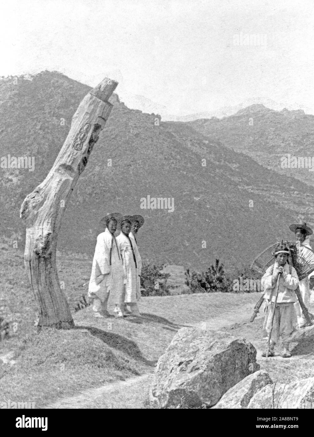 Fotografia mostra il gruppo di coreani in abito tradizionale in piedi vicino a un post scolpito su una strada di montagna. Posti 1920-1924 scolpite per mantenere i diavoli dal passante Foto Stock