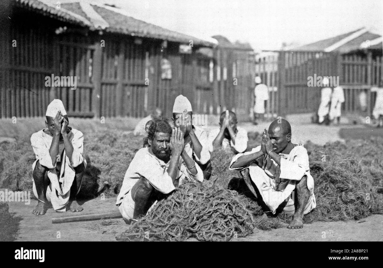 Fotografia mostra cinque detenuti maschi squatting con mani premuti insieme nel mezzo di un materiale fibroso a Rangoon, Birmania 1910-1920 Foto Stock