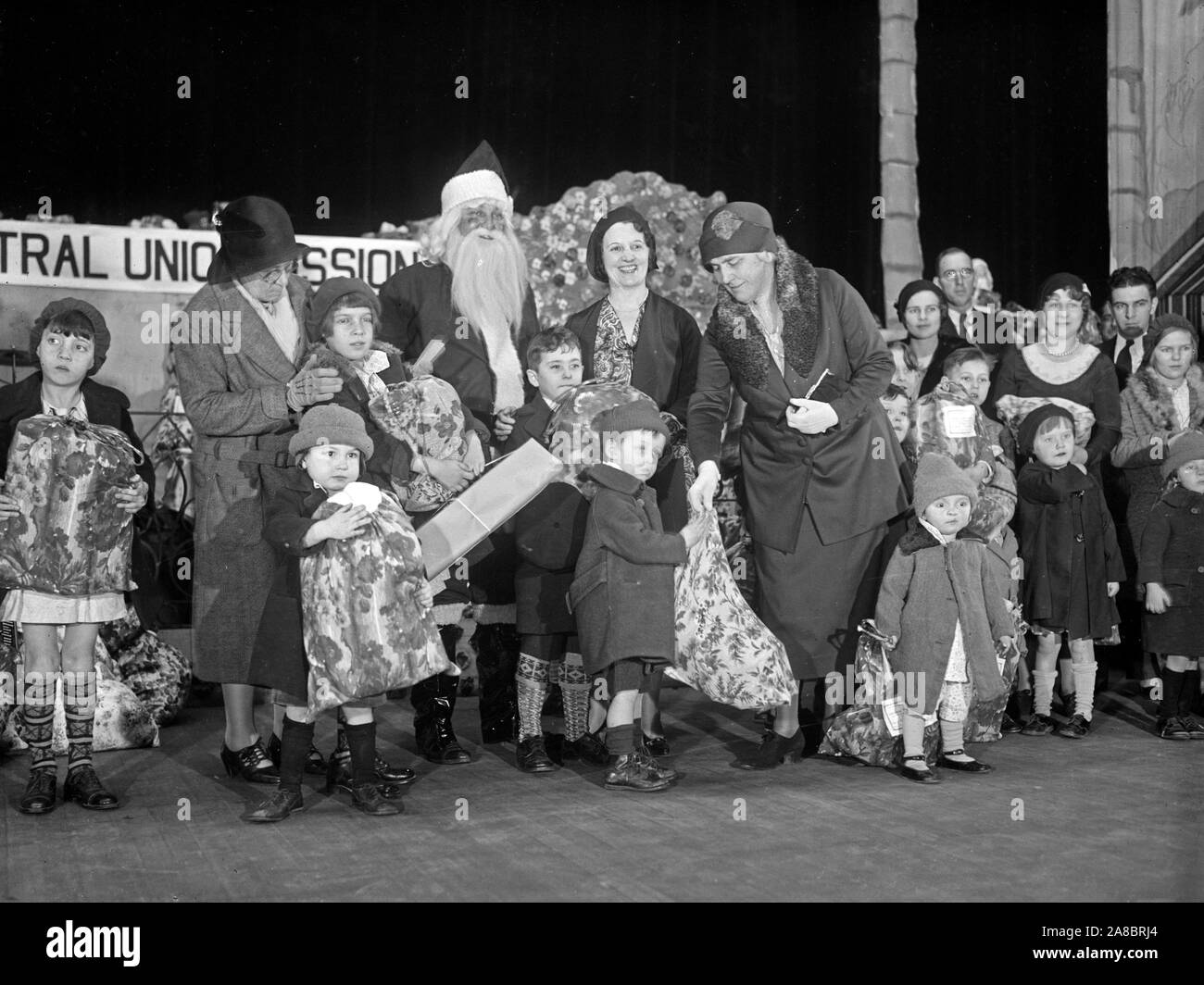 Ella è mostrato di consegnare uno dei 1.500 sacchetti di cibo e regali che erano state distribuite dall'Unione centrale missione in un partito svoltasi nel Teatro Fox. Assistere la signora Hoover sono Santa Claus, nella persona di Giovanni S. Bennett, e la Sig.ra Bennett, che hanno la responsabilità della missione. 12/24/30 Foto Stock