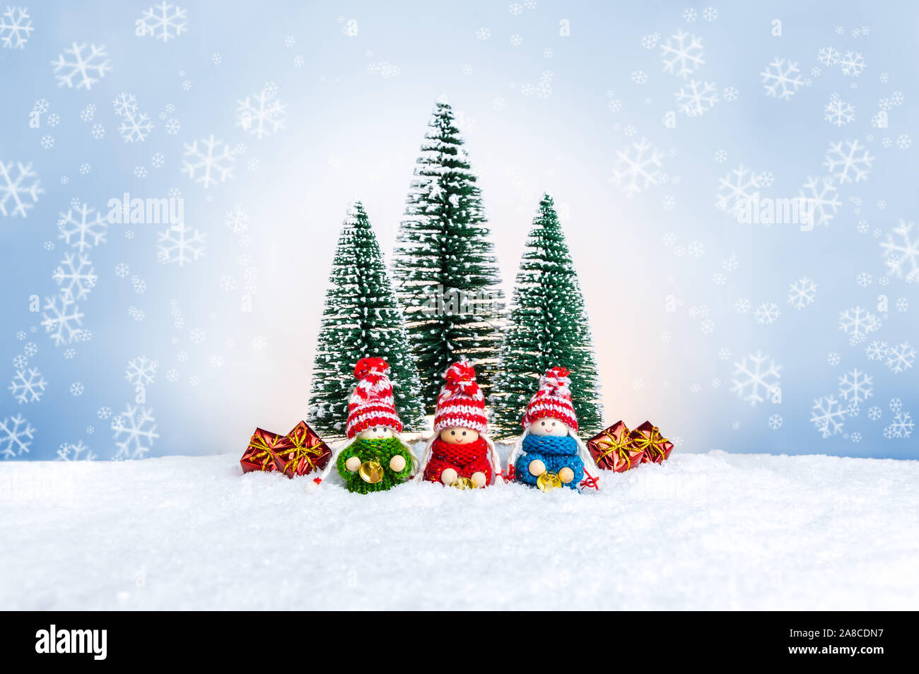 Bambole di maglia come piccoli bambini in un colorato maglioni holding campane nei pressi di abeti e presenta. Carino il Natale figure come una vacanza fatta a mano decoratio Foto Stock