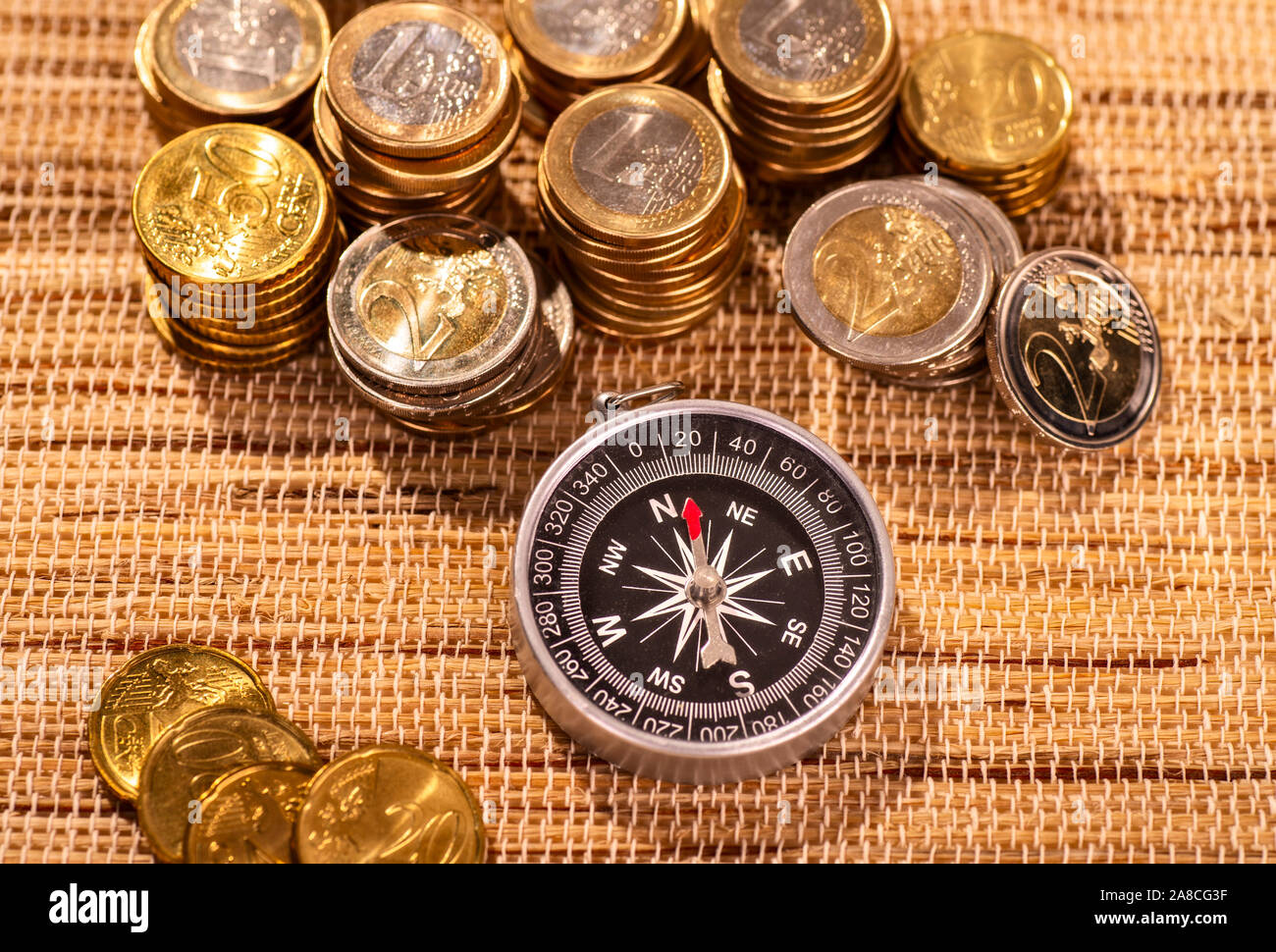 Pile di monete in euro con una bussola in primo piano Foto Stock