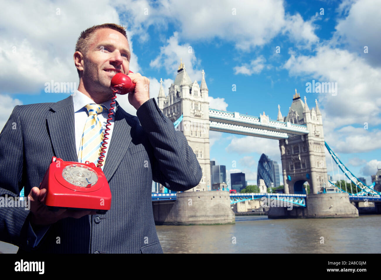 L'uomo d'affari britannico ascolta la buona nuova hotline su un vecchio telefono rotante rosso di fronte allo skyline di Londra al Tower Bridge Foto Stock
