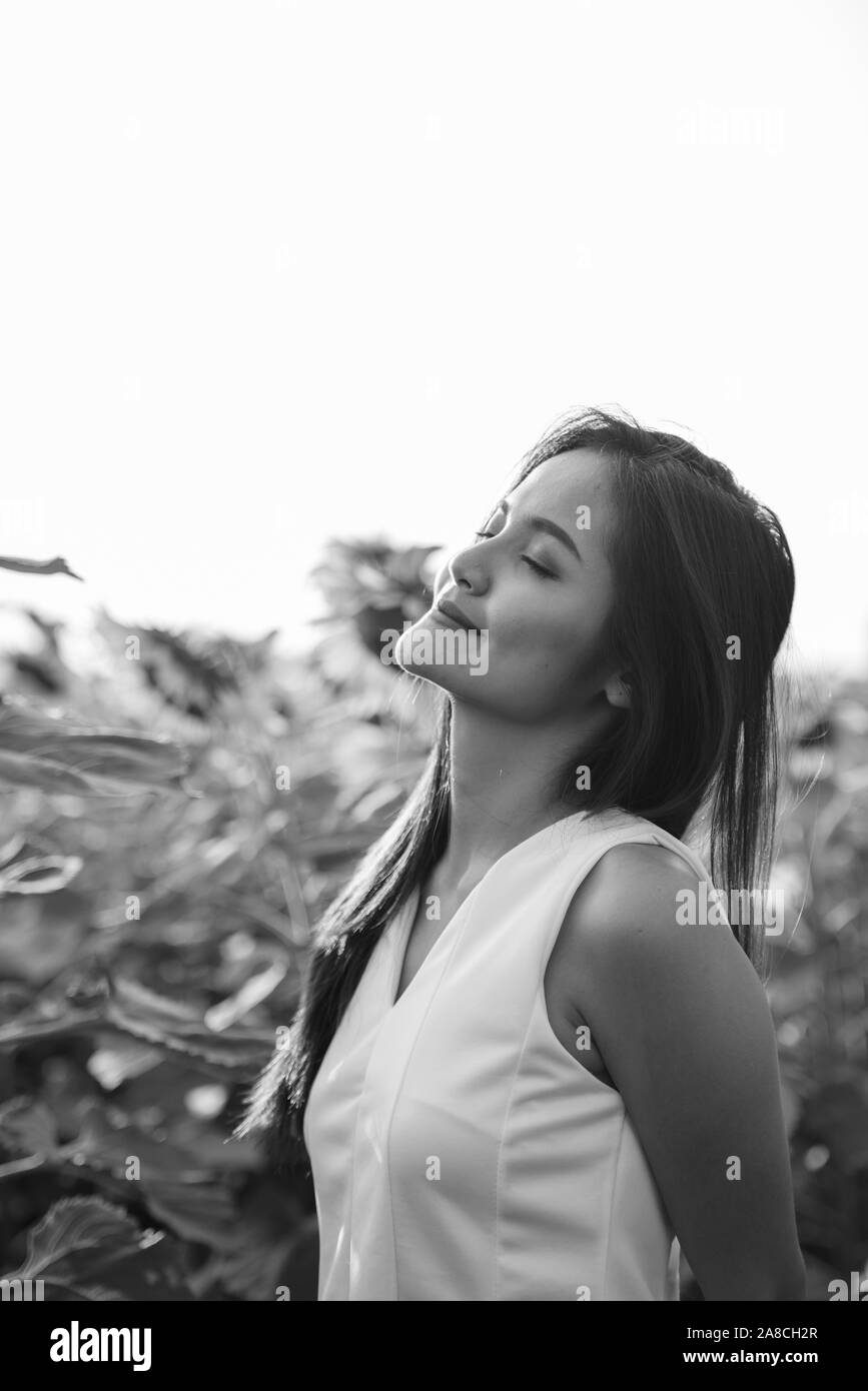 Giovane bella donna asiatica con gli occhi chiusi nel campo di girasoli in fiore Foto Stock