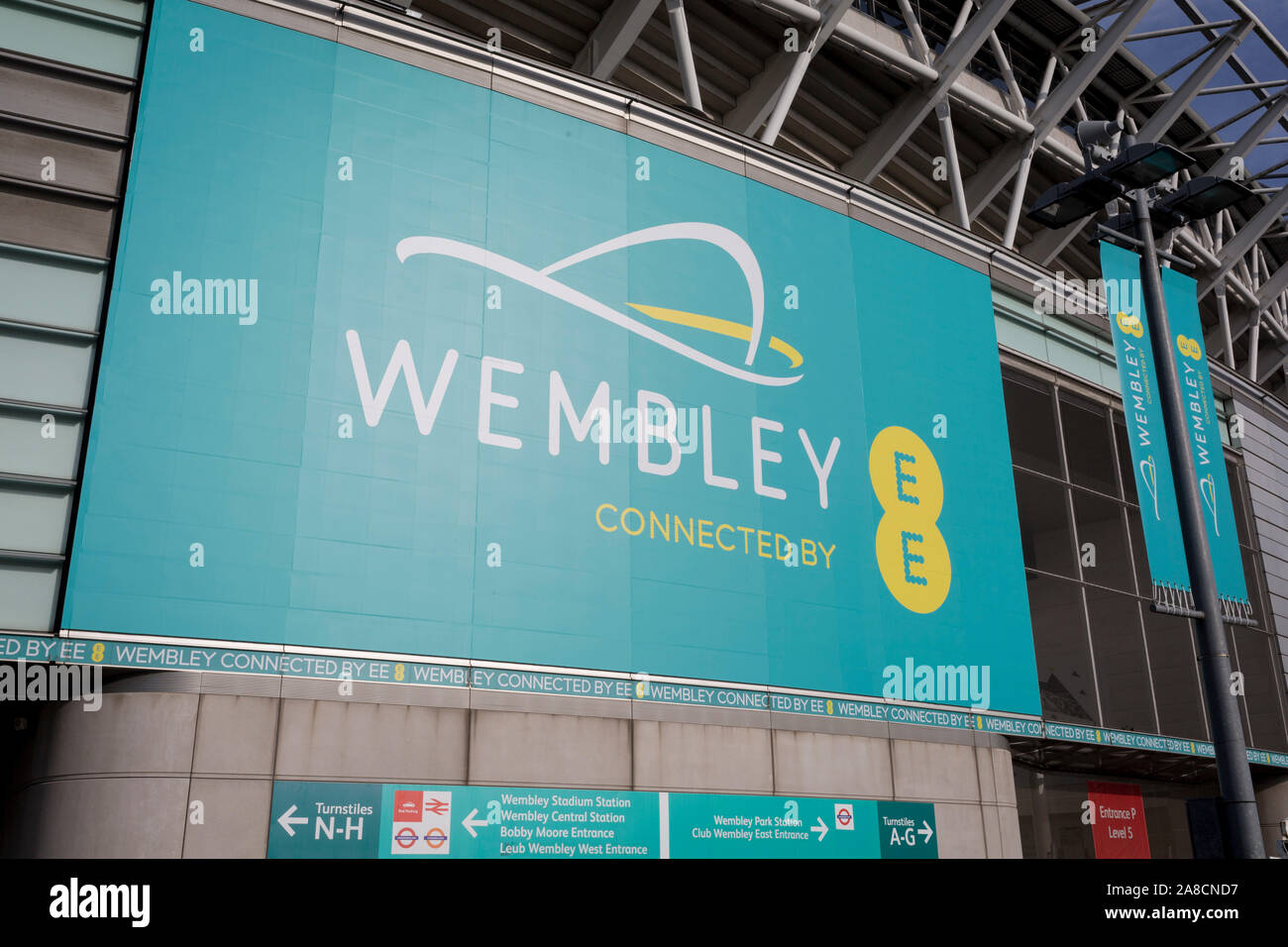 Un banner per lo stadio di Wembley e il marchio di comunicazioni EE, il 6 novembre 2019, a Wembley, Londra, Inghilterra. Lo stadio di Wembley è mobile app e interattivo di un sistema di illuminazione a LED sull'arco che può rispondere ai gol, folla rumore più provando i pagamenti contactless e biglietti con lo scopo di rendere più del 50% dei pagamenti contactless. Nel 2018, il mondo il primo live evento sportivo per essere trasmesso su 5G utilizzati remote production. Foto Stock